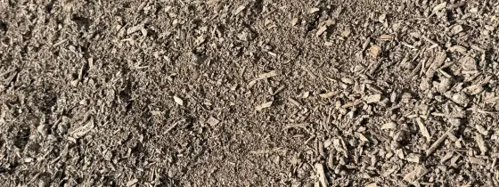 Composta cernida fina gris-café extendida al sol, con pequeños trozos de fibra de madera