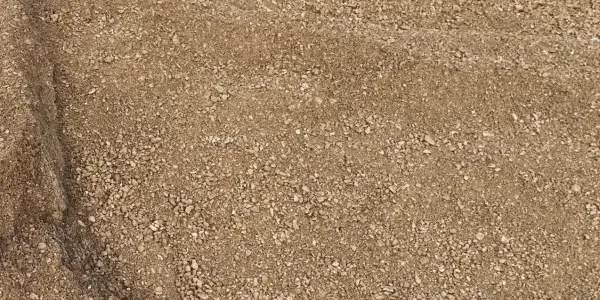 Pile of tan decomposed granite at the Casco Organics yard, fine grit with small pale stones and a shaded fold at the left