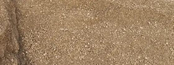 Pila de granito descompuesto color arena en la yarda de Casco Organics, grano fino con piedritas claras y un pliegue en sombra a la izquierda