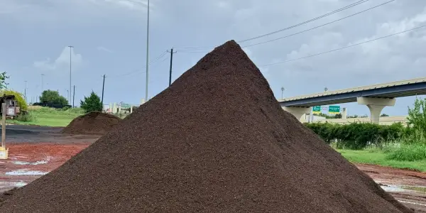 Pila alta de Garden Mix café oscuro en la yarda de menudeo, con una pila más chica y el puente de la autopista atrás bajo un cielo nublado