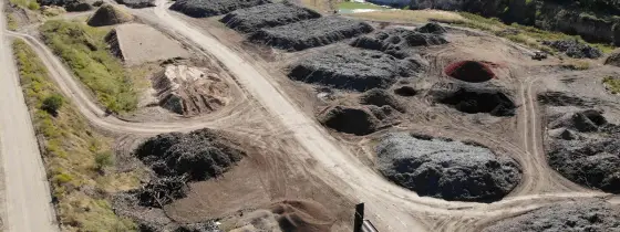 Vista aérea de la yarda de Casco Organics con hileras de pilas de mulch, una criba y camiones, y un estanque al fondo