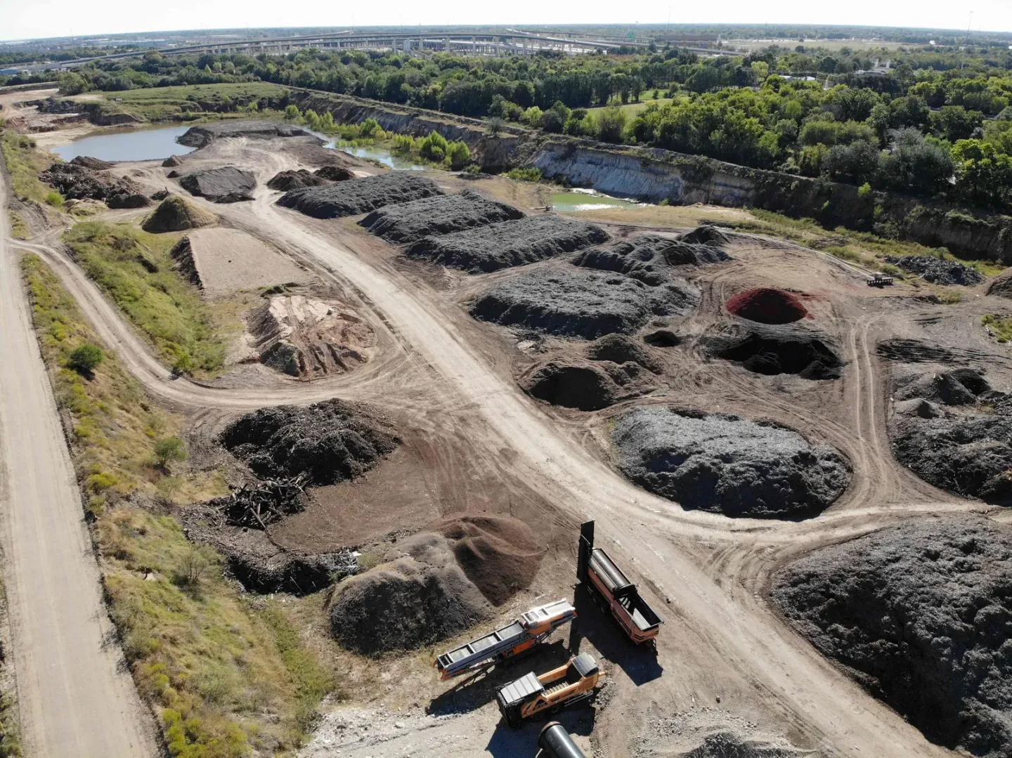 Vista aérea de la yarda de Casco Organics con hileras de pilas de mulch, una criba y camiones, y un estanque al fondo