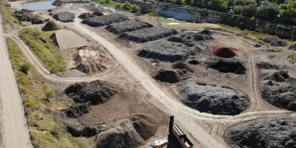 Aerial view of the Casco Organics yard with rows of dark mulch piles, a screener and trucks, and a pond beyond