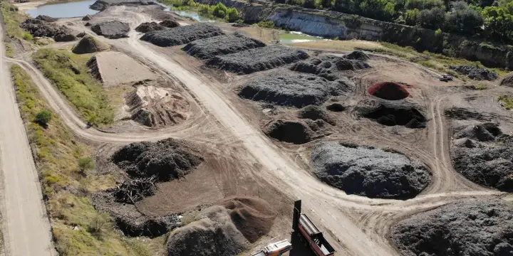 Vista aérea de la yarda de Casco Organics con hileras de pilas de mulch, una criba y camiones, y un estanque al fondo