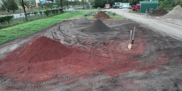 Aerial of a bright red mulch pile in the Casco Organics retail yard, with darker piles and the gravel road beyond