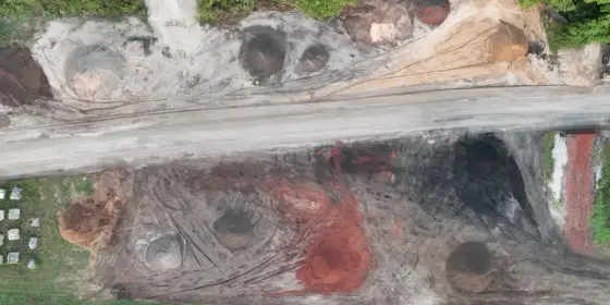 Vista desde arriba de la yarda de menudeo de Casco Organics partida por un camino de grava, con pilas de material rojo, negro y café a ambos lados y árboles arriba
