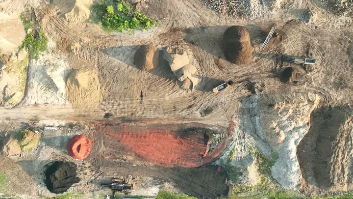 Vista aérea directo hacia abajo de la yarda de producción de Casco Organics: hileras de composta, mulch rojo, pilas de arena y madera, y equipo en los caminos